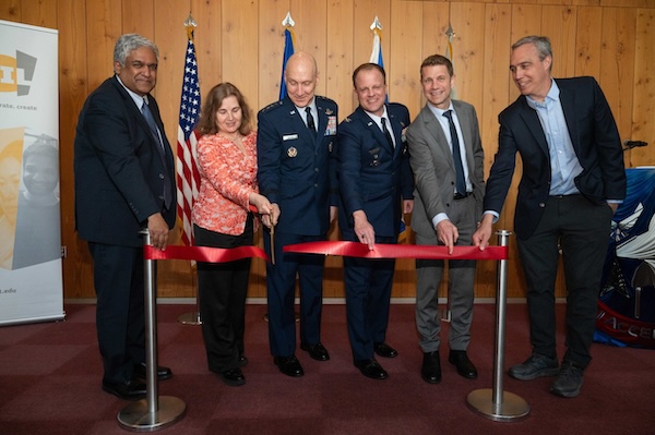Six people stand in front of a red ribbon while one person holds a pair of scissors.
