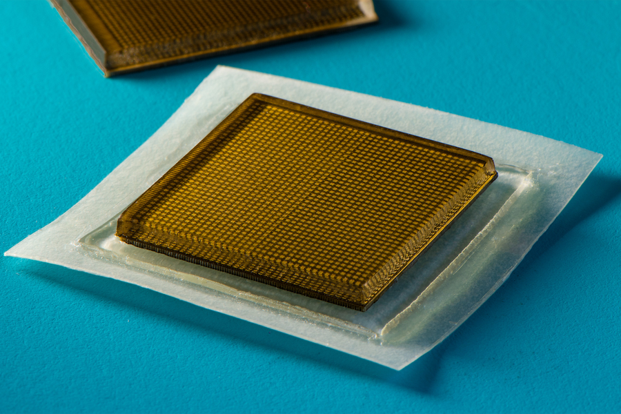 A close-up of a small square amber-colored adhesive patch with a grid texture, placed on a white backing against a teal surface.