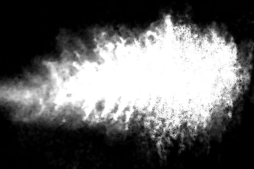 High-contrast black and white scientific image of a bright white diffuse plume or particle cloud expanding against a black background, representing nanoscale material behavior research.