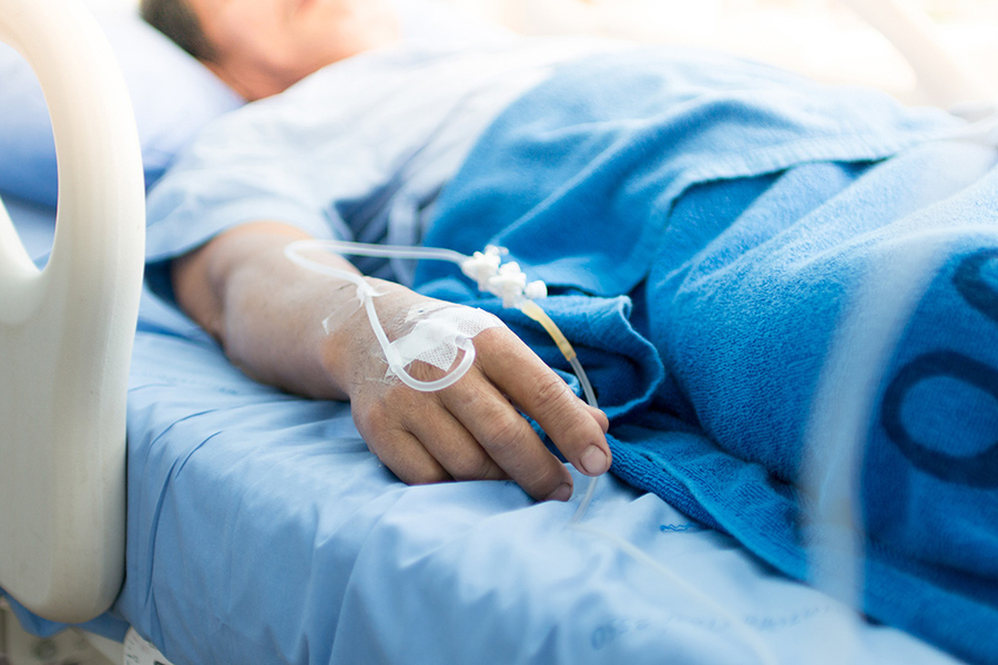 A close-up of a patient's hand with an IV line resting on a blue hospital blanket.